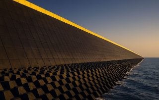Tanggul raksasa pantai Jawa dengan susunan tetrapod dan dinding beton modern, dipotret sudut dramatis saat cahaya lembut senja menyinari garis pantai utara.